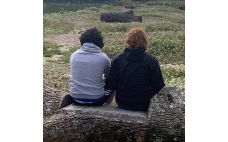 The backs of two people sitting on a stone plnth