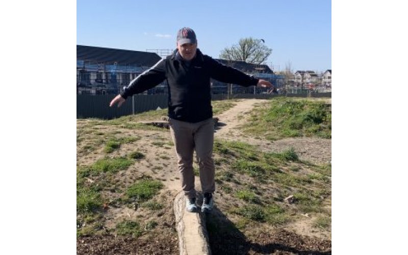Older man balancing on wooden beam outside