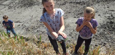 Three kids in front of a dried out water channel with one kid holding a turtle