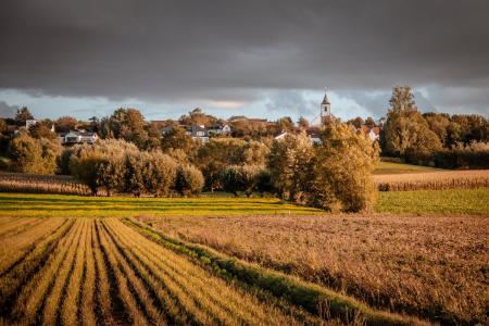 sun in cloudy grey sky shining onto green fields