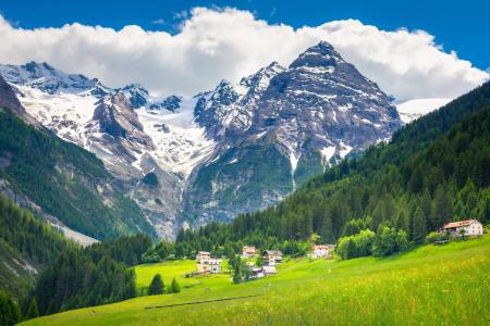 swiss alps - green rolling moutains with snow capped mountains in the distance, blue sky and fluffy white clouds - sunny day