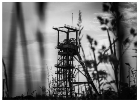 An industrial tower shown through blades of grass.