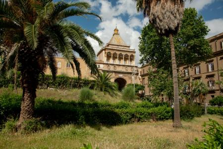 An old building in Palmero with palm trees and grass in front of it.