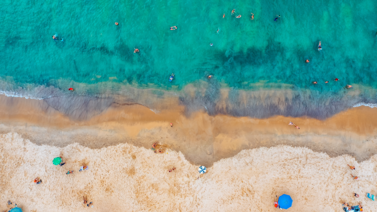 Aerial image of a beach and seashore with people enjoying the beach.