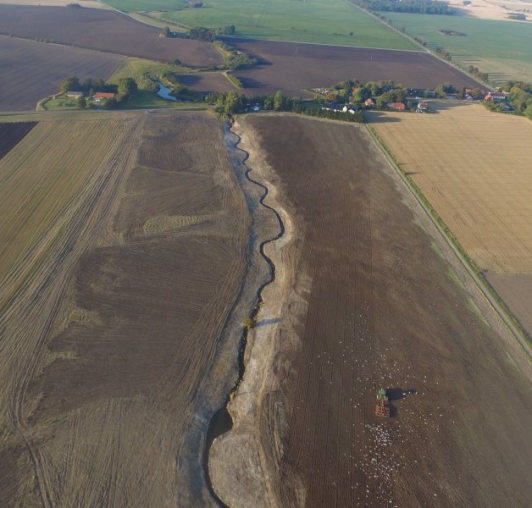 A sinuous stream corridor running through ploughed agricultural land.