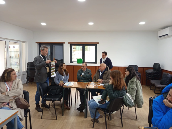 Person holding a poster during a workshop session with participants sitting around tables listening to the person. 