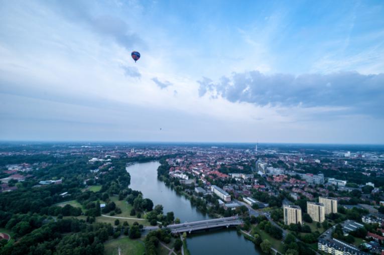 View of Muenster with the river running through the middle of the city. There is a hot air balloon in the sky. 