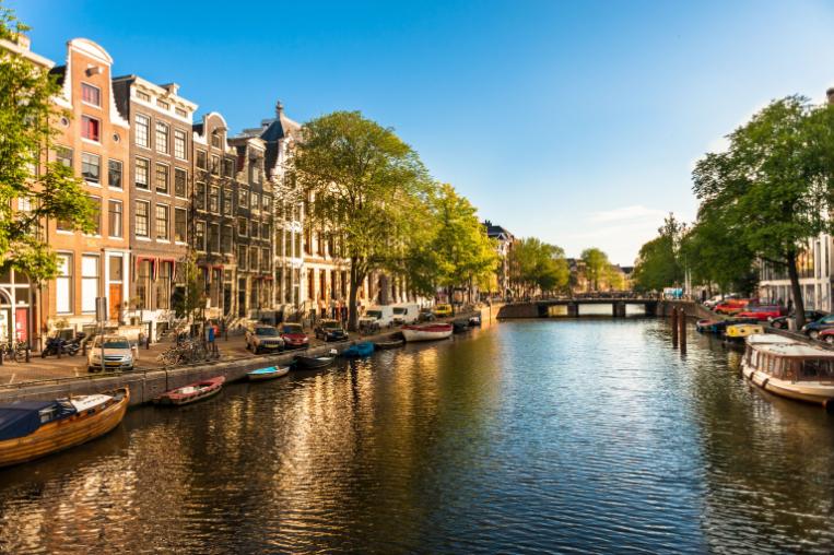 The canal flowing through Amsterdam, there are buildings on either side and a bridge crosses the canal.