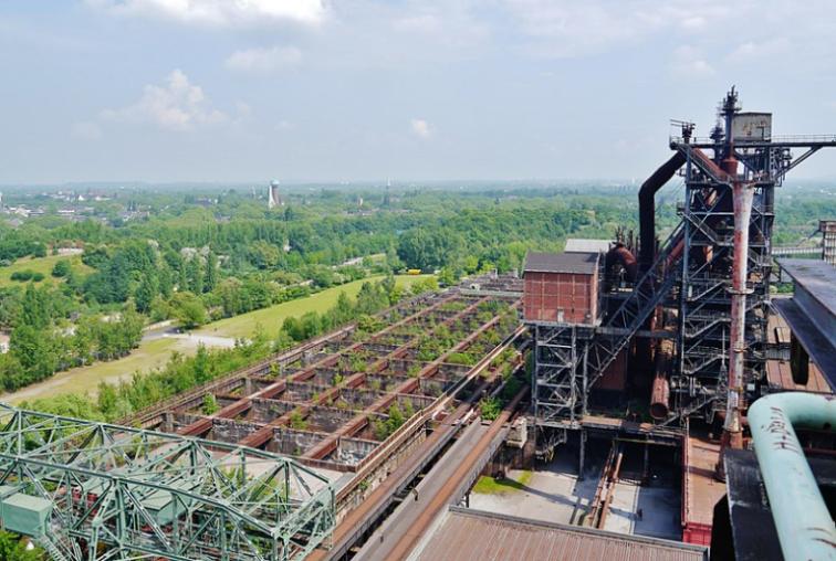 A derelict industrial site which has been taken over by nature, the roof has fallen in and plants are growing inside and around the building.