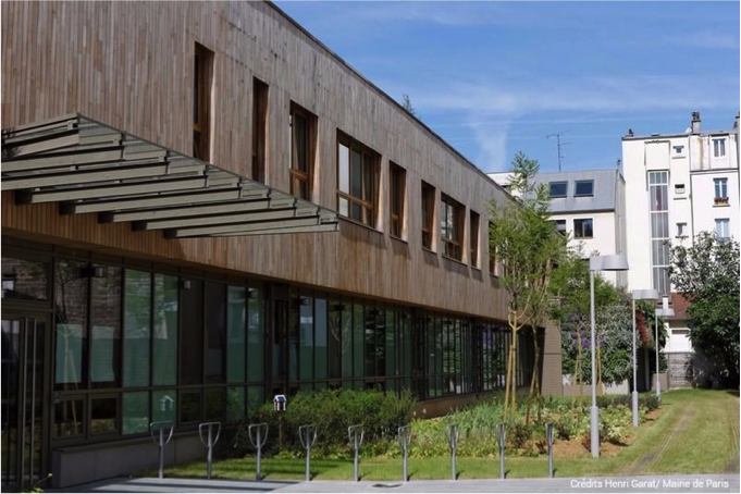 The wooden facade of a school with an extensive greenspace in front of it.