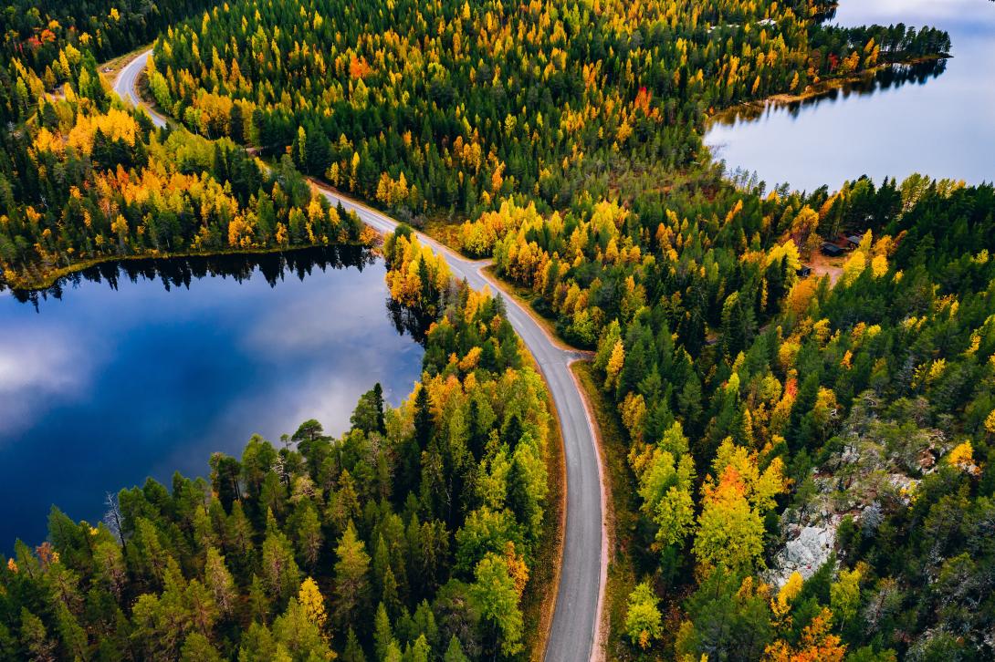 Aerial view of road and forest with mountains and blue lakes in Finland